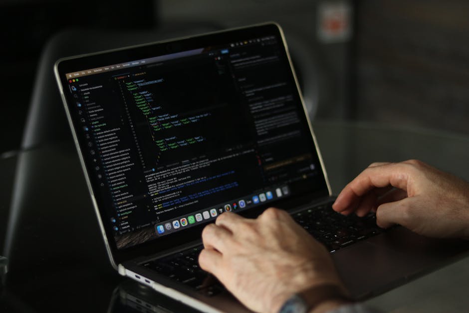 A close-up view of a laptop with a black casing and a backlit keyboard featuring red illumination, displaying lines of code on its screen with a blurred background. Positioned to the right of the lapt